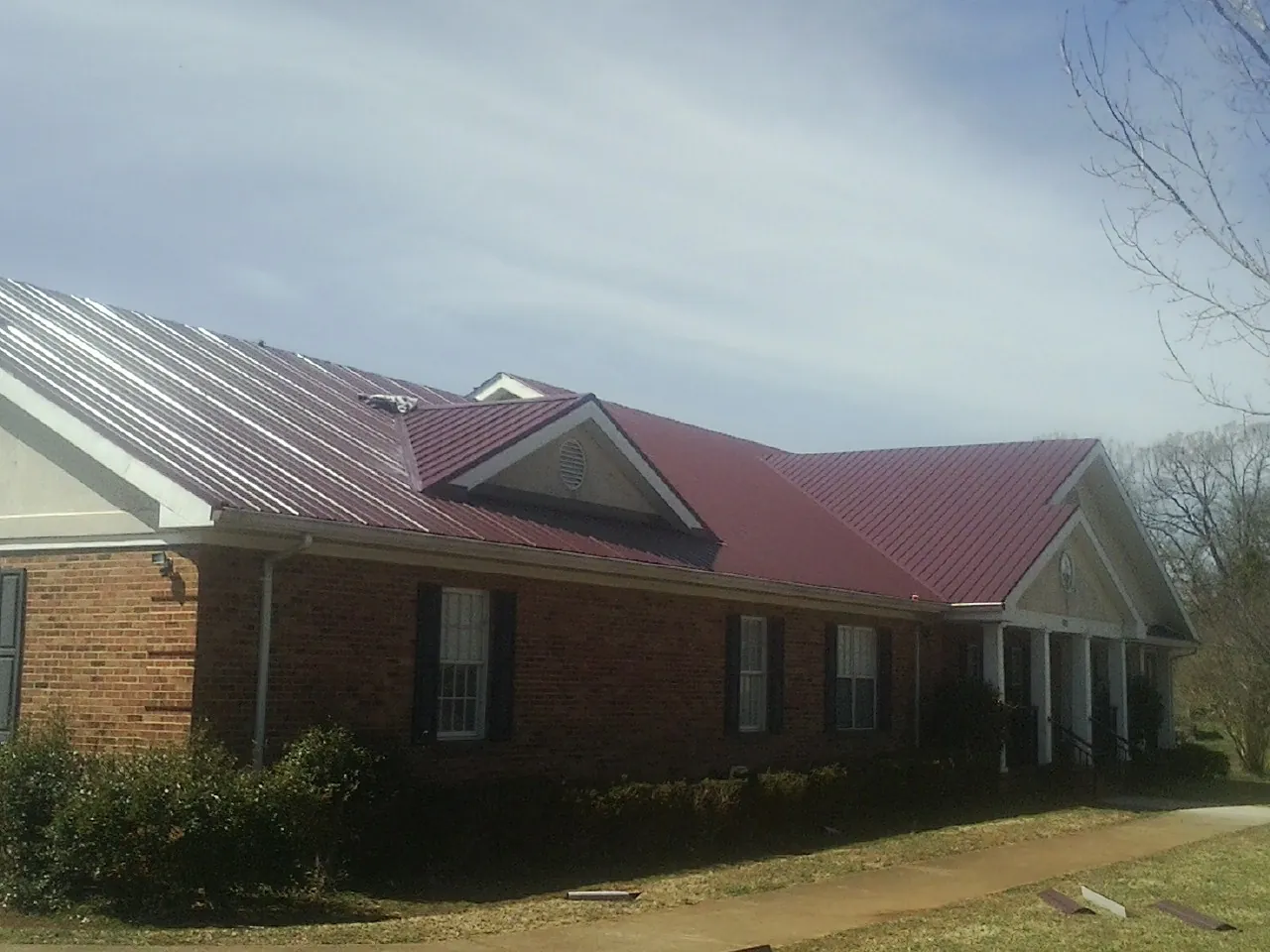 Red metal roof with gabled entries on a long brick building, from a Hail Damage Roof Repair job in Randallstown