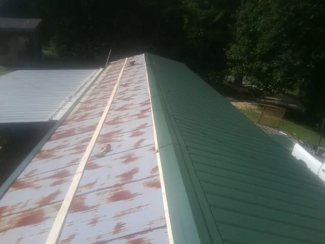 Old rusted panels beside newly installed green metal roofing — Wind Damage Roof Repair by Roofing Brothers in Randallstown