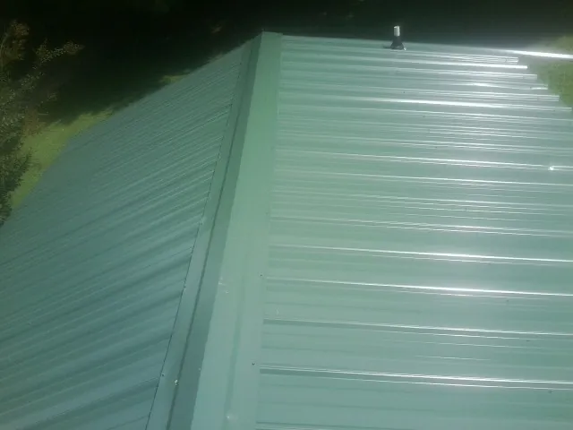 New green metal panels meeting at the ridge of a roof — Flat Roof Repair work by our crew in Randallstown