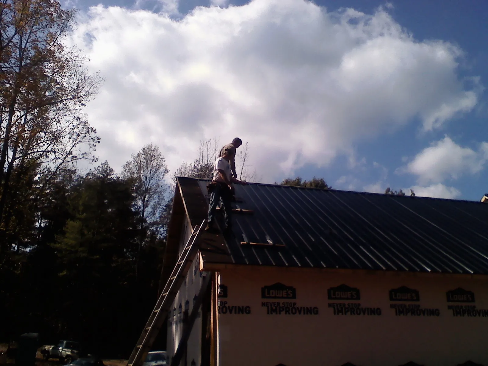Roofer fastening dark metal panels high against a cloudy sky, from a Roof Inspection job in Randallstown