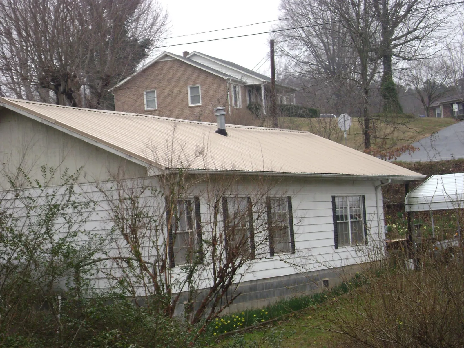 Tan metal roof on a white sided house set into a hillside — Commercial Roofing by Roofing Brothers in Randallstown